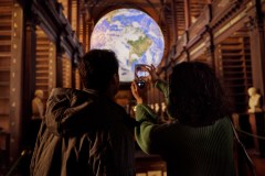 Two people taking a photograph of Gaia in the Long Room