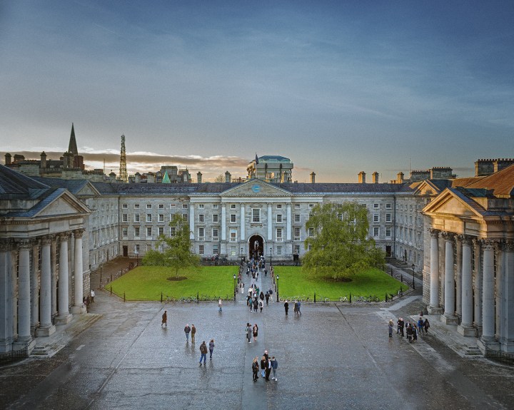A blue sky over historical buildings with small clusters of people on a grey square