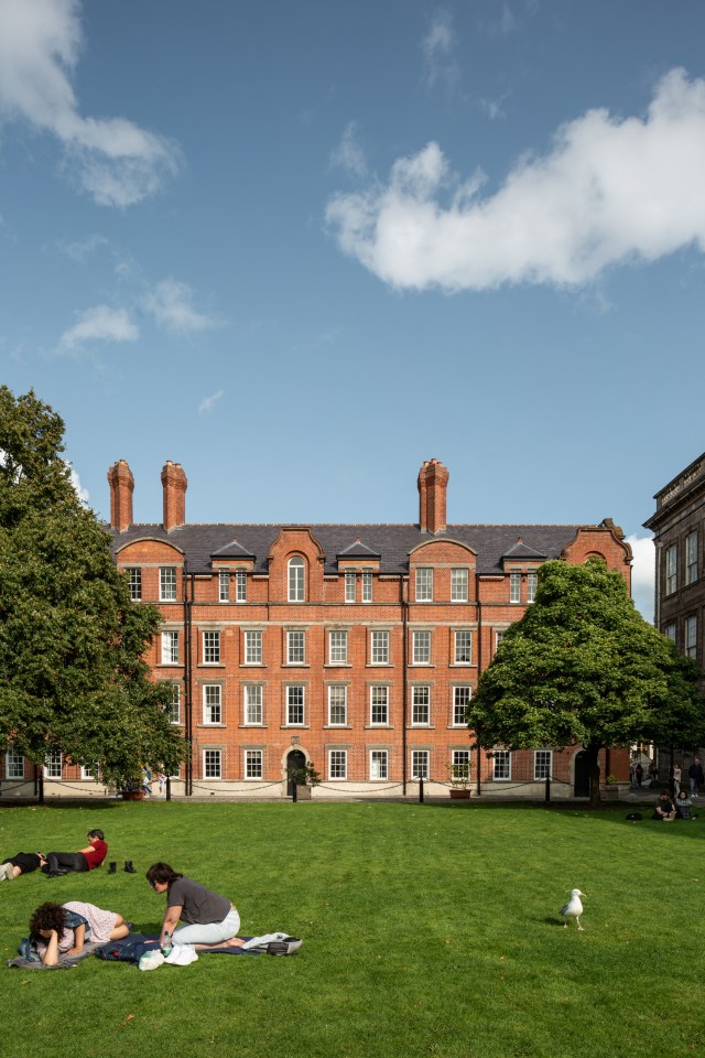 Image of students lying out on the grass of Trinity College, with a red-brick building in the background